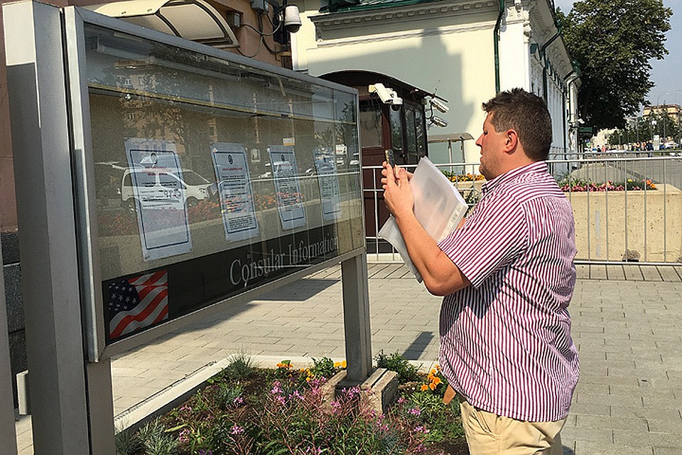 Посетитель фотографирует документы на стенде возле посольства США.