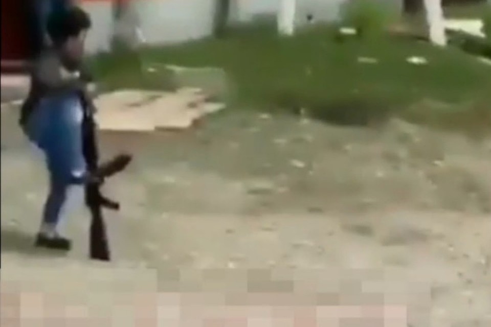 Мальчик перезаряжает автомат ногой, направив дуло в голову