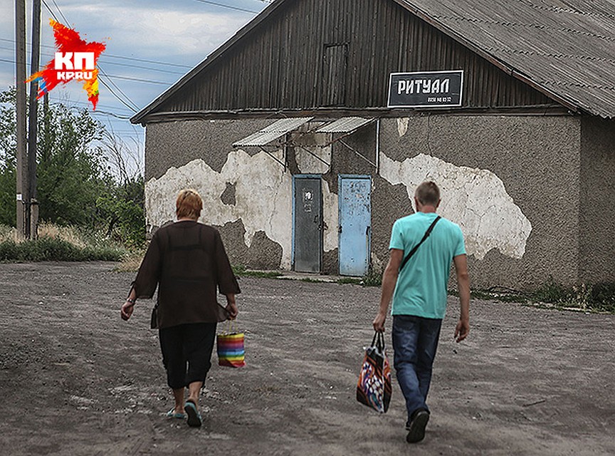 Местные жители идут мимо таблички «Ритуальные услуги», пока за их спинами громыхают взрывы